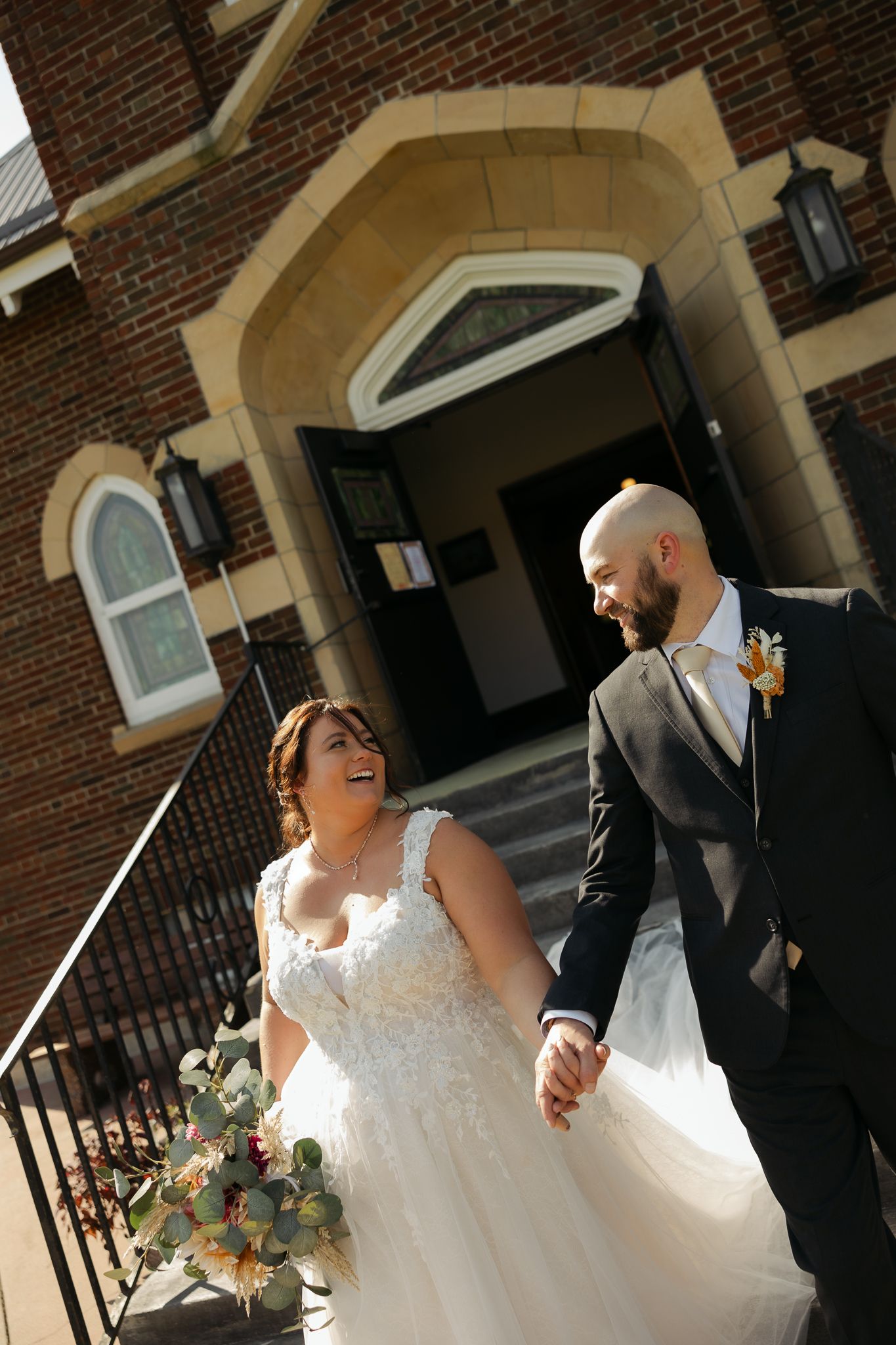 Happy couple walking outside brick building entrance in formal wedding attire.