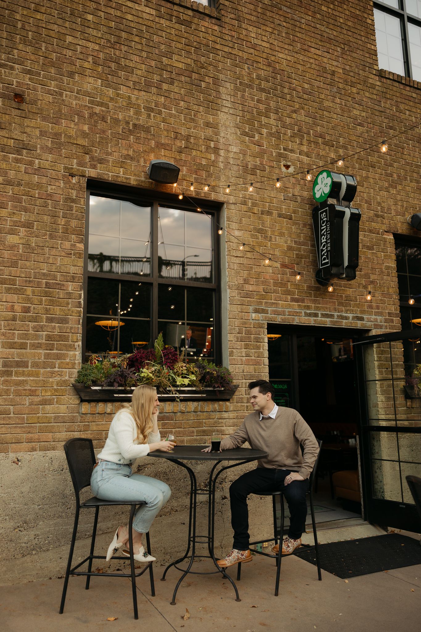 Couple sitting at outdoor cafe tables against brick wall exterior.