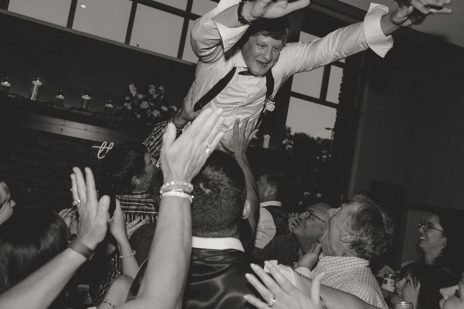 Crowd of party guests dancing with raised arms at an indoor celebration.