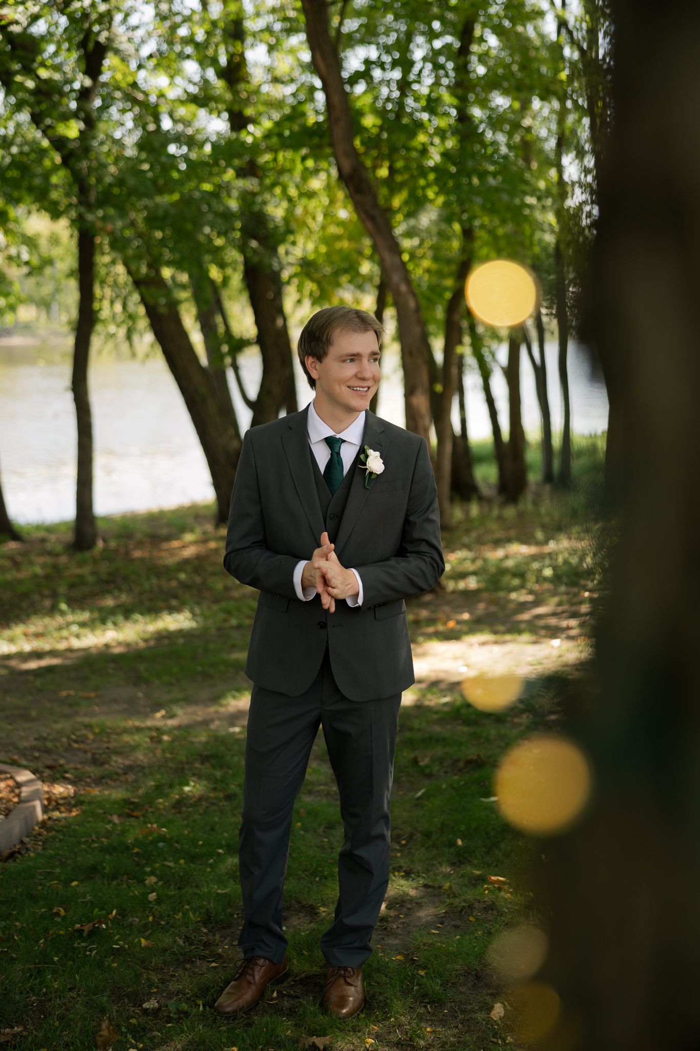 A wedding couple shares a joyful moment in a sunlit wooded area with bokeh light effects.