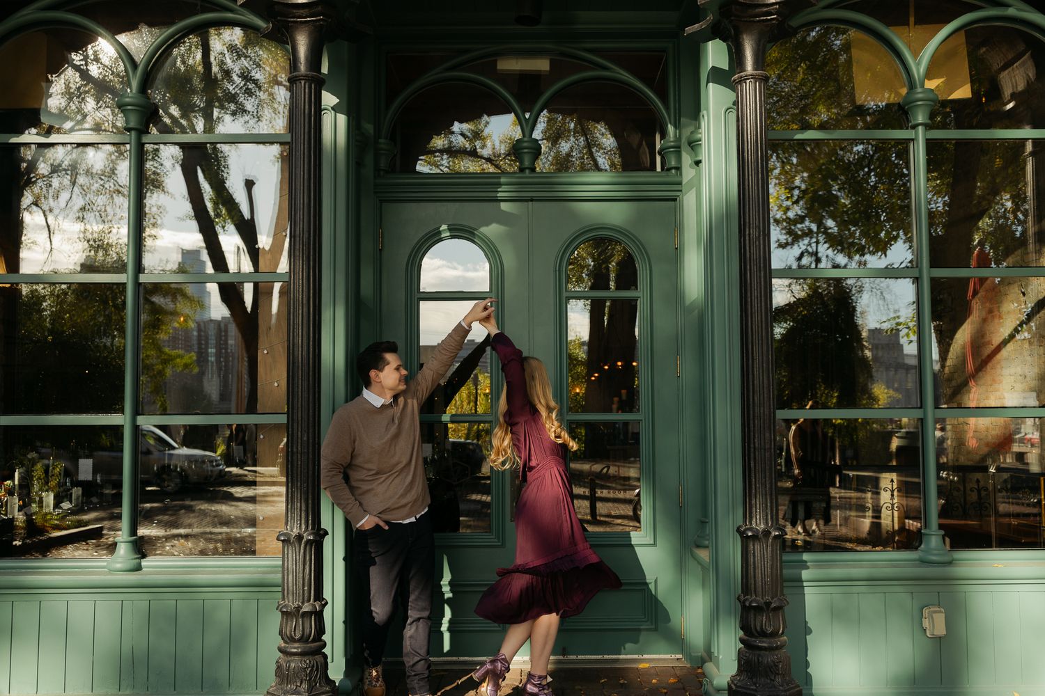 Two people standing together outside a historic building with green trim and large windows.