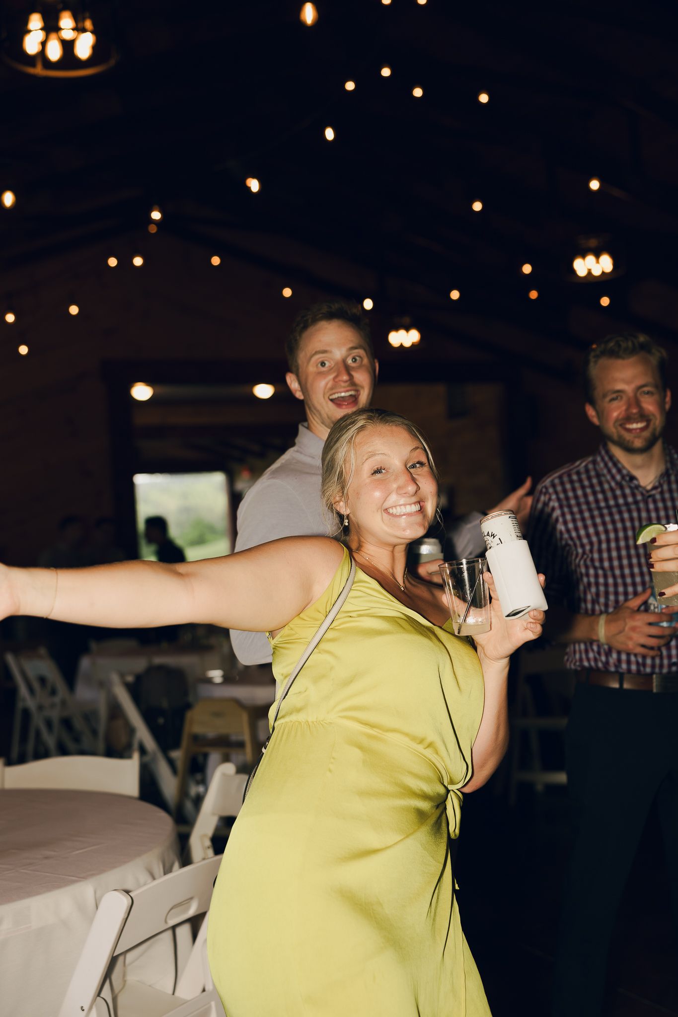 Person in yellow dancing enthusiastically under decorative string lights at an indoor venue.