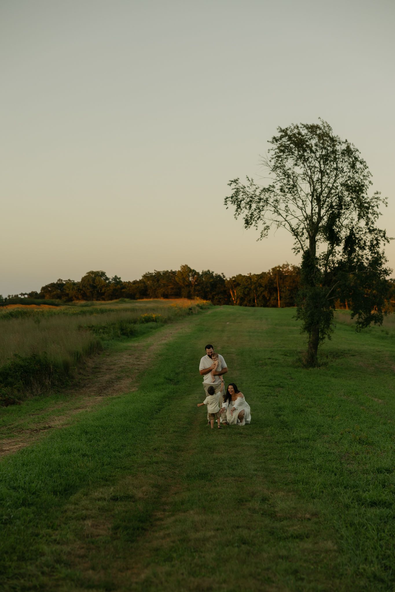 A couple sits together on grass during sunset in a rural field.