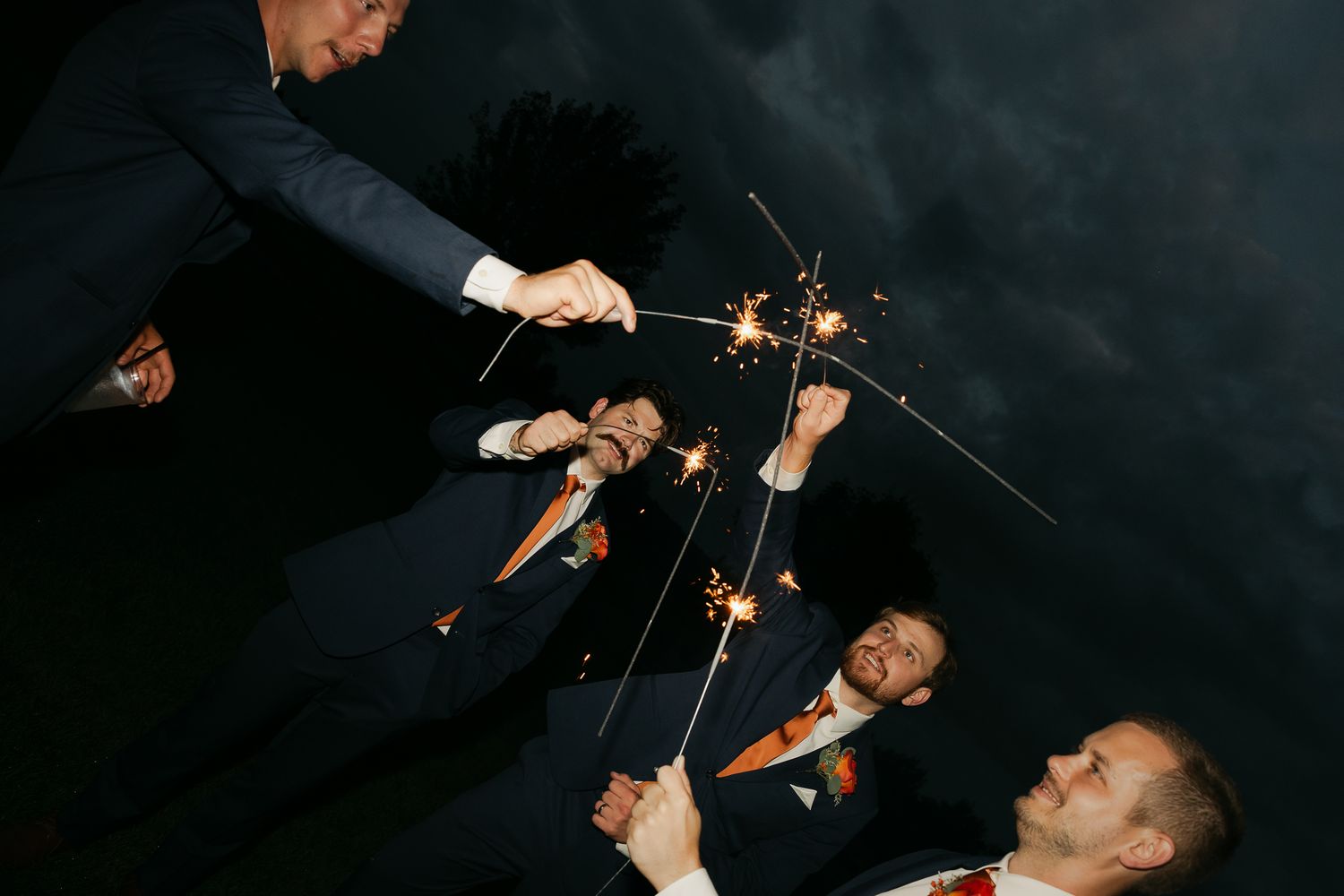 Wedding guests wave sparklers creating light trails in the dark.