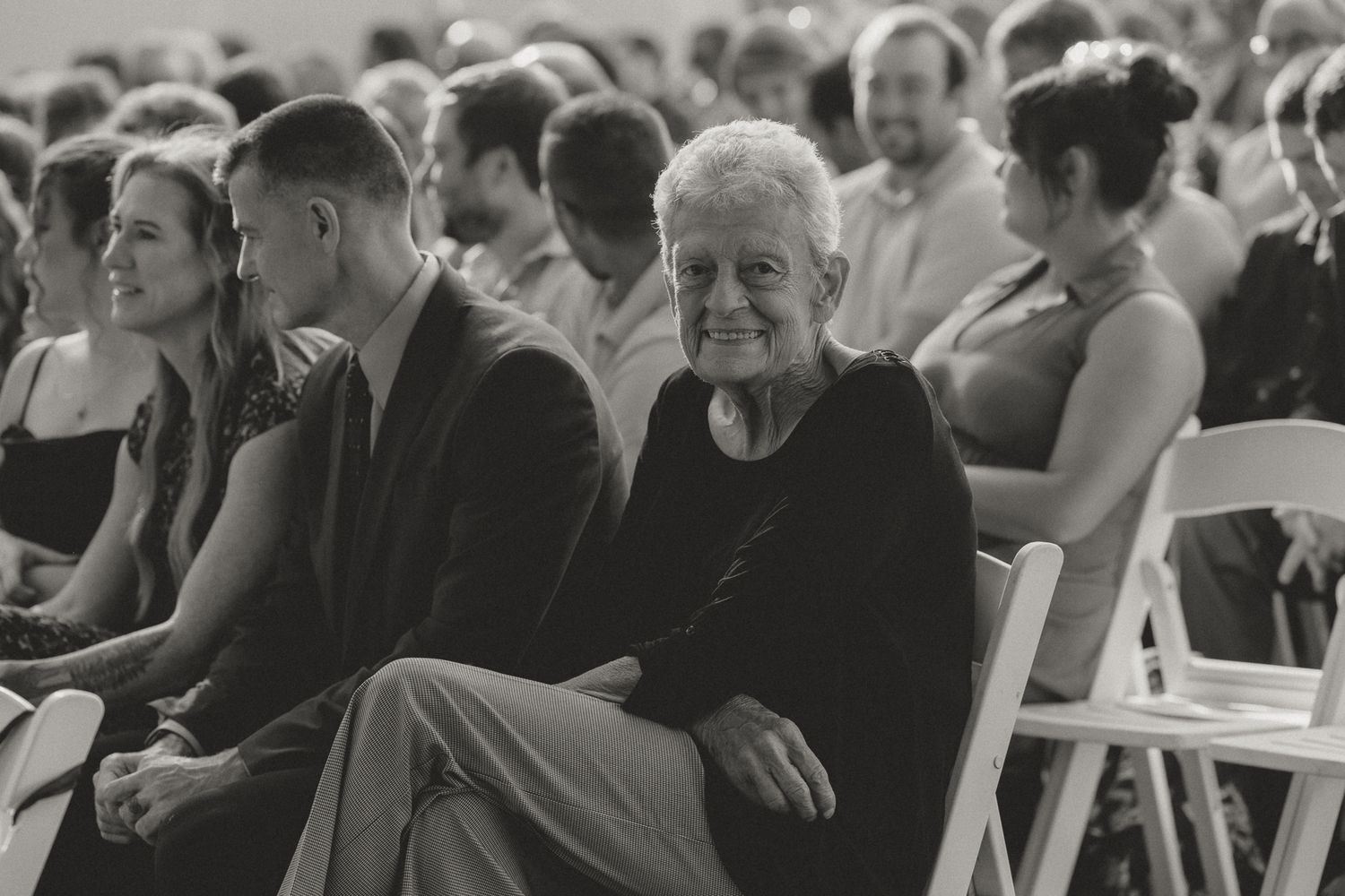 Wedding ceremony guests seated in white chairs watching the proceedings.