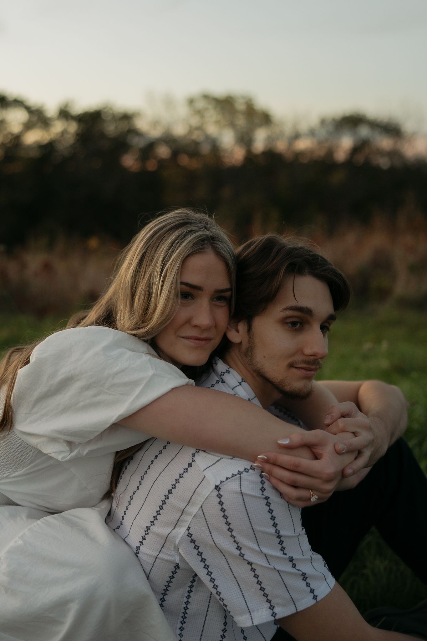 Tender embrace captured in soft evening light on a grassy hillside.