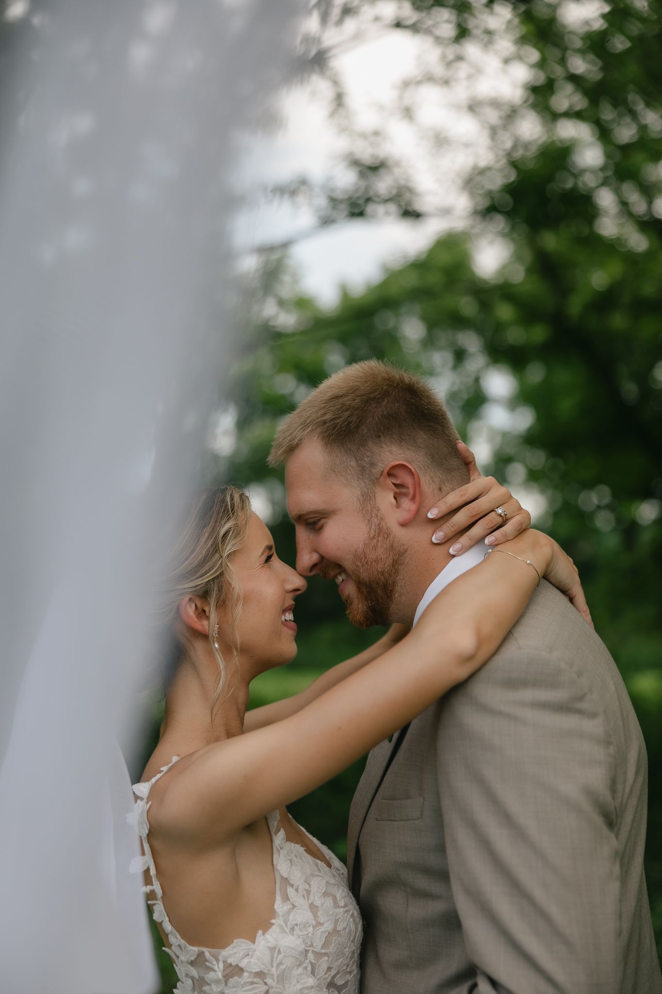 An intimate wedding portrait captured through a veil in a natural outdoor setting.