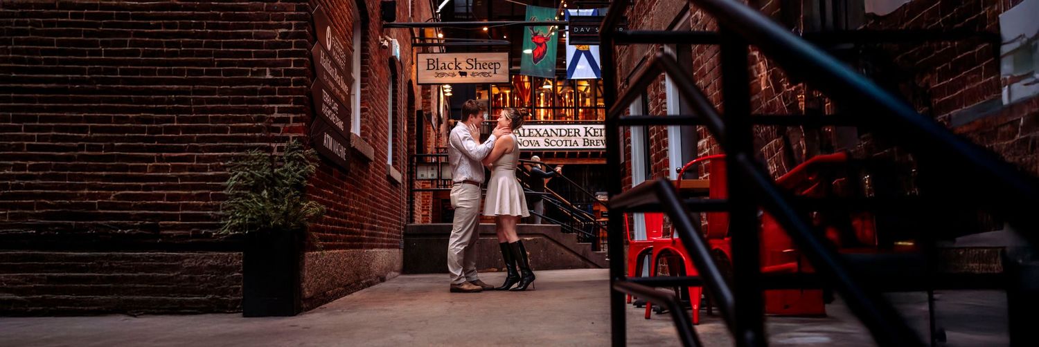 Couple dancing romantically on a dimly lit urban alley at night, surrounded by brick buildings and glowing city signs.