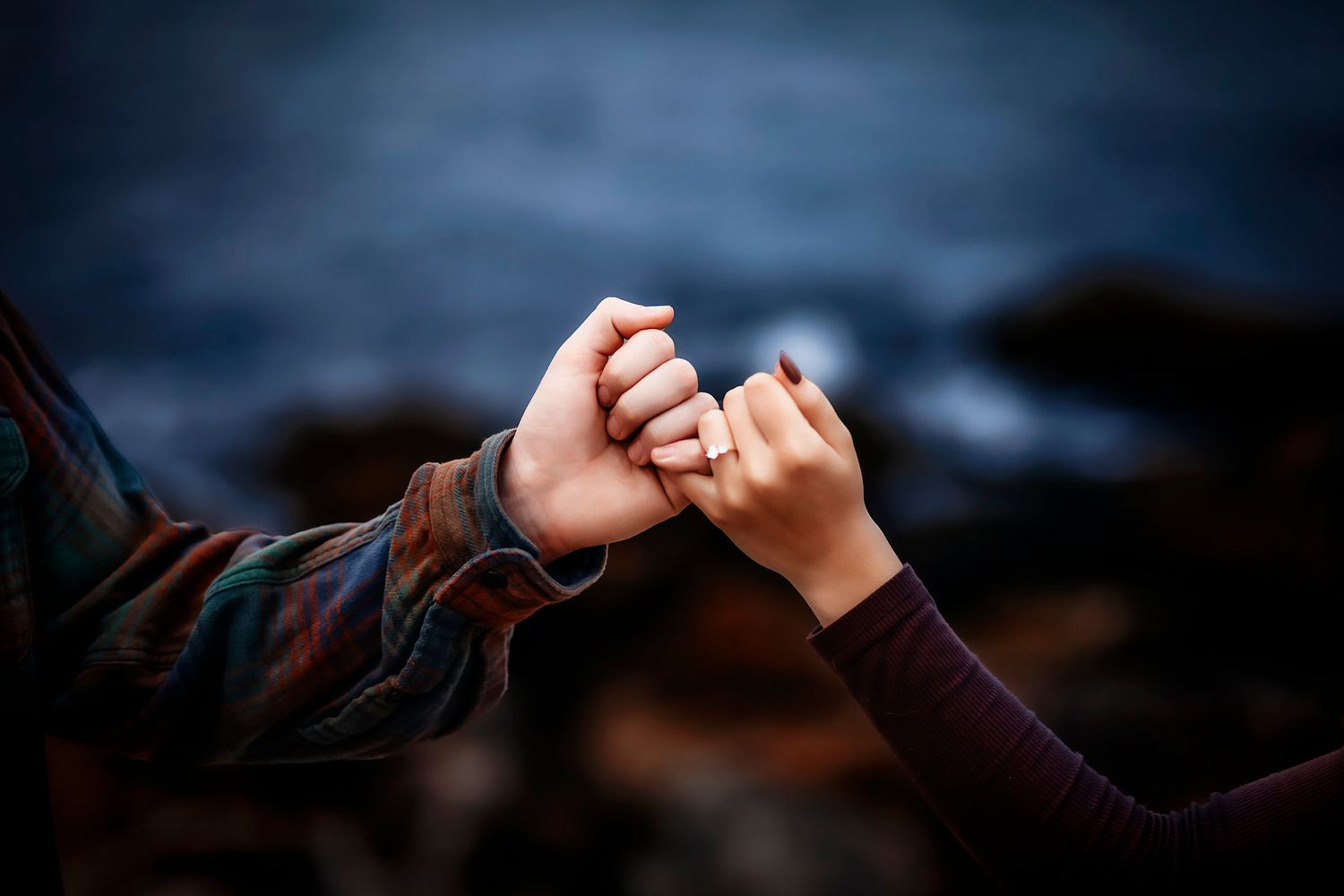 Two people holding hands near the ocean, one wearing a ring, symbolizing love and connection.