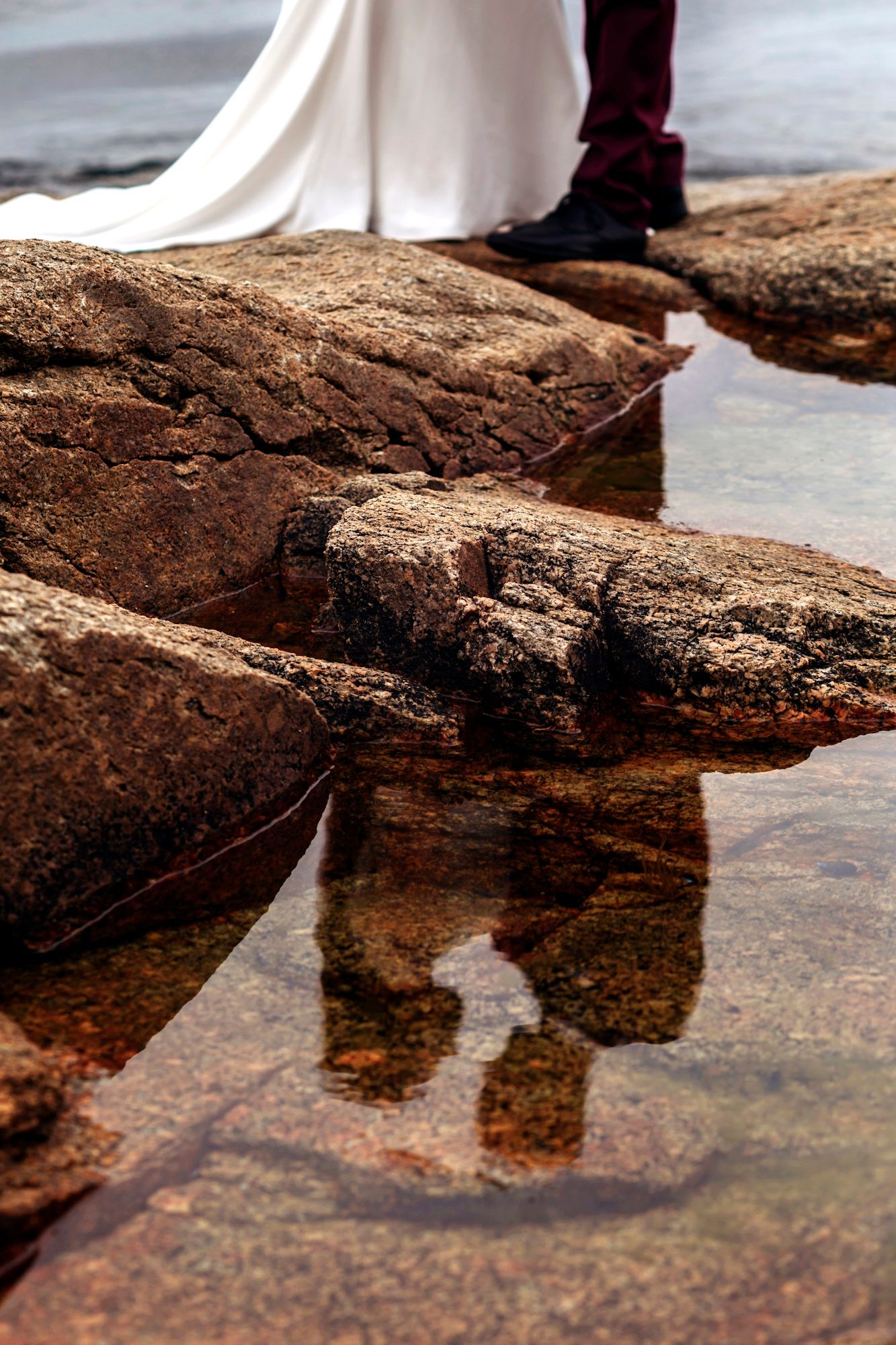 Chester ns Bride and groom standing on rocky shoreline with their reflection visible in a tidal pool below.