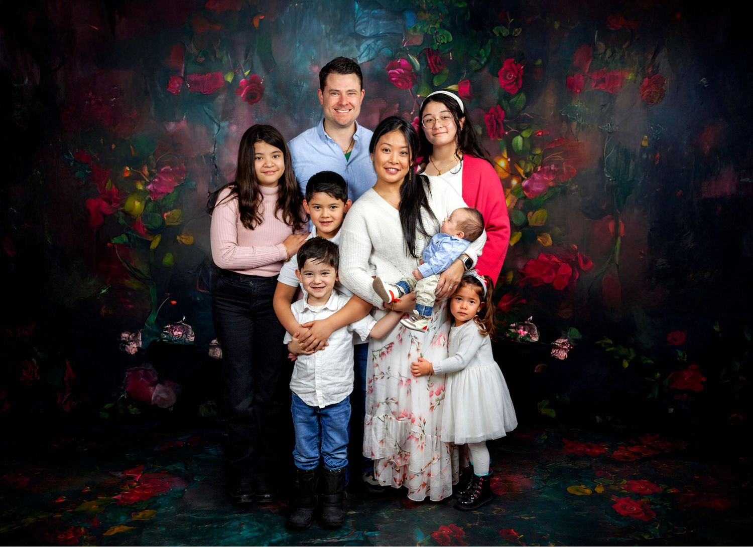 Family portrait of parents with five children posing in front of a floral painted backdrop.