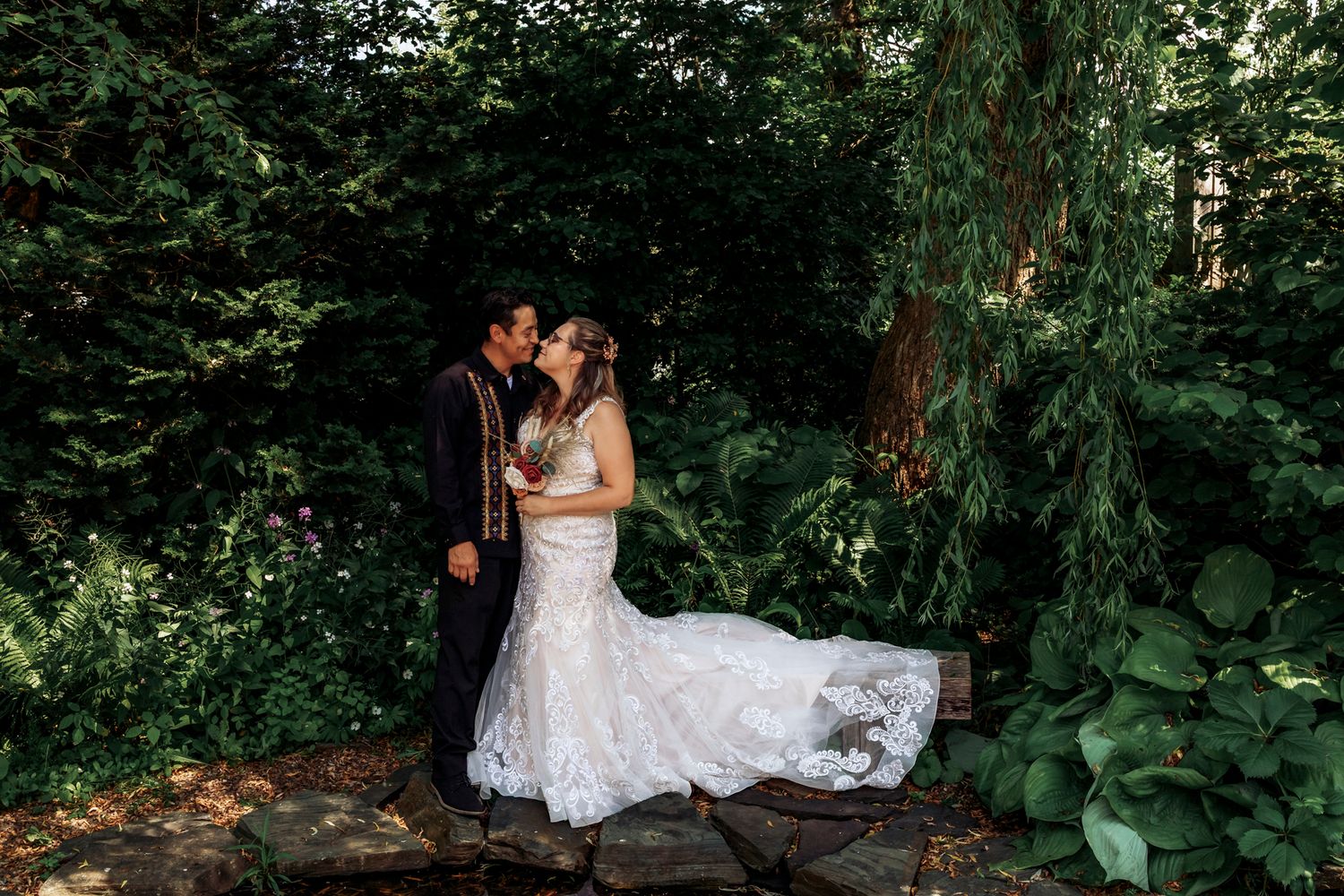 Bride and groom share a romantic moment in a lush garden setting, surrounded by green trees and foliage.