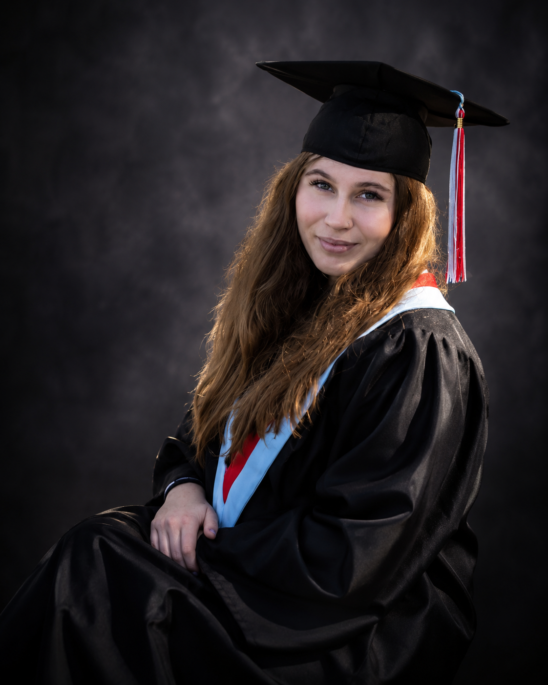 Young woman in black graduation gown and cap with colorful tassel smiles for a professional portrait photo.