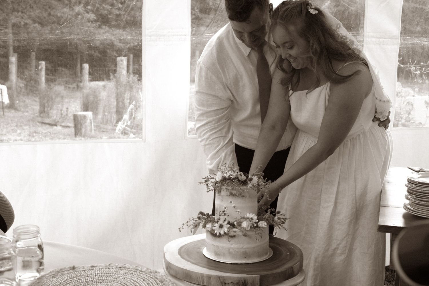 Bride and groom cutting their wedding cake together in a romantic black and white photo.