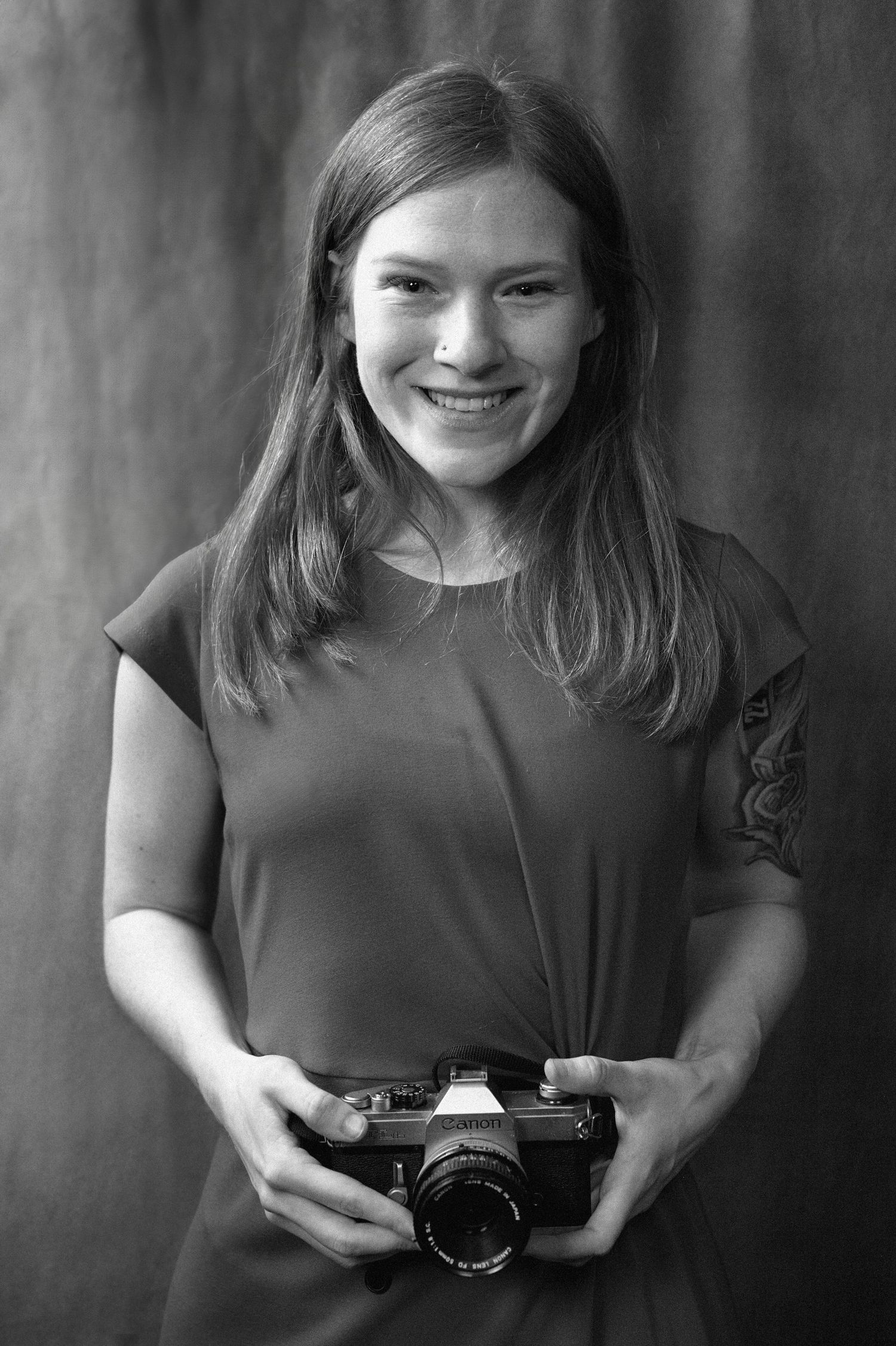 Smiling young woman with long hair holding a vintage film camera, black and white portrait photo.
