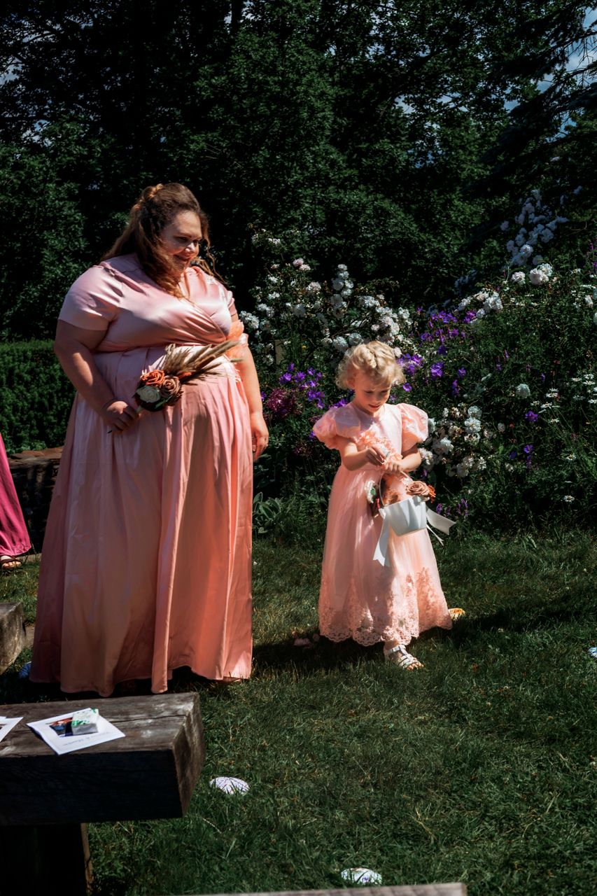 Woman and flower girl in matching peach dresses at an outdoor garden wedding ceremony.