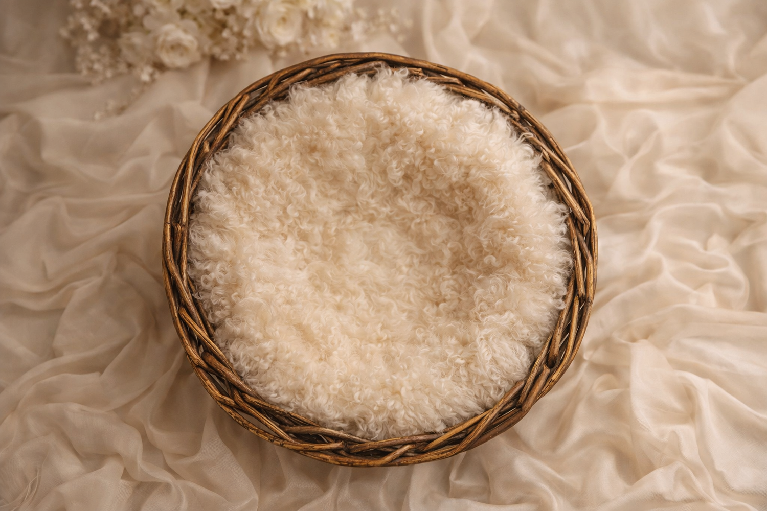 A wicker basket lined with soft white fluffy fabric on cream draped cloth for newborn photography.