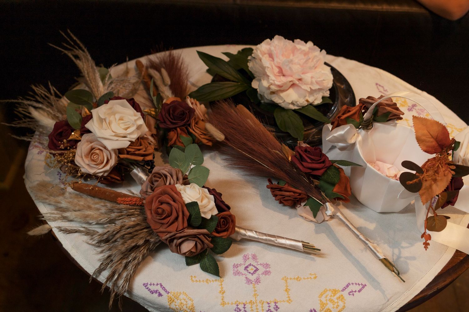 Elegant dried floral arrangements with brown roses, feathers, and cream blooms displayed on a white decorative tray.