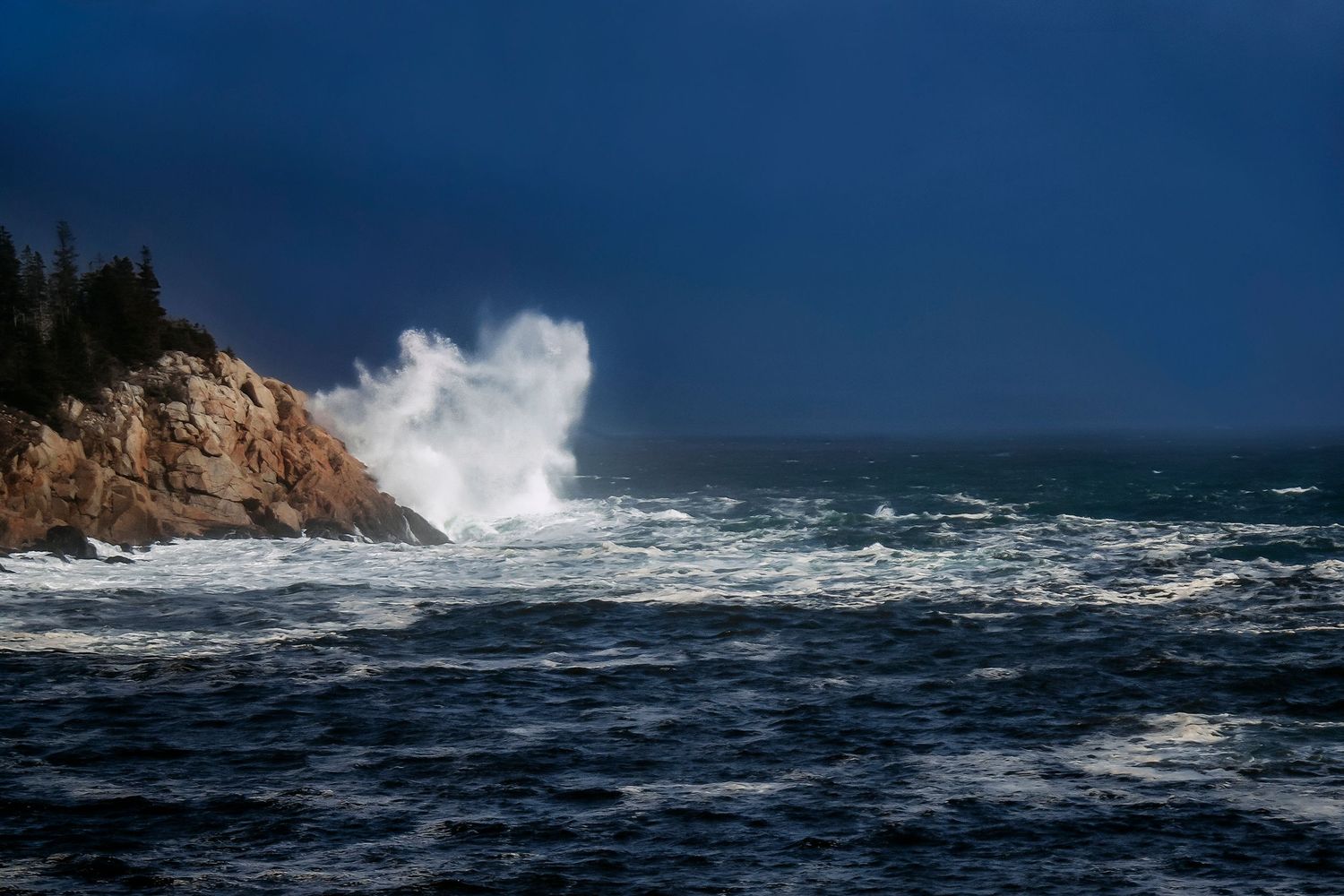 Dramatic ocean waves crashing against rocky coastline cliffs under a stormy dark blue sky.