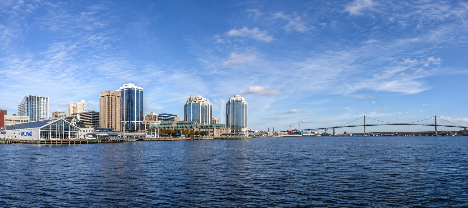 Panoramic waterfront view of Norfolk, Virginia skyline with modern buildings and bridge under blue skies.