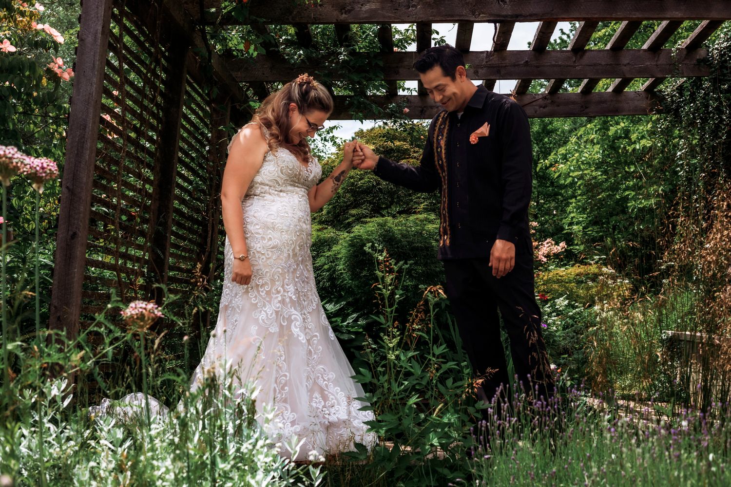 Bride and groom share a tender moment under a garden pergola, surrounded by lush greenery on their wedding day.