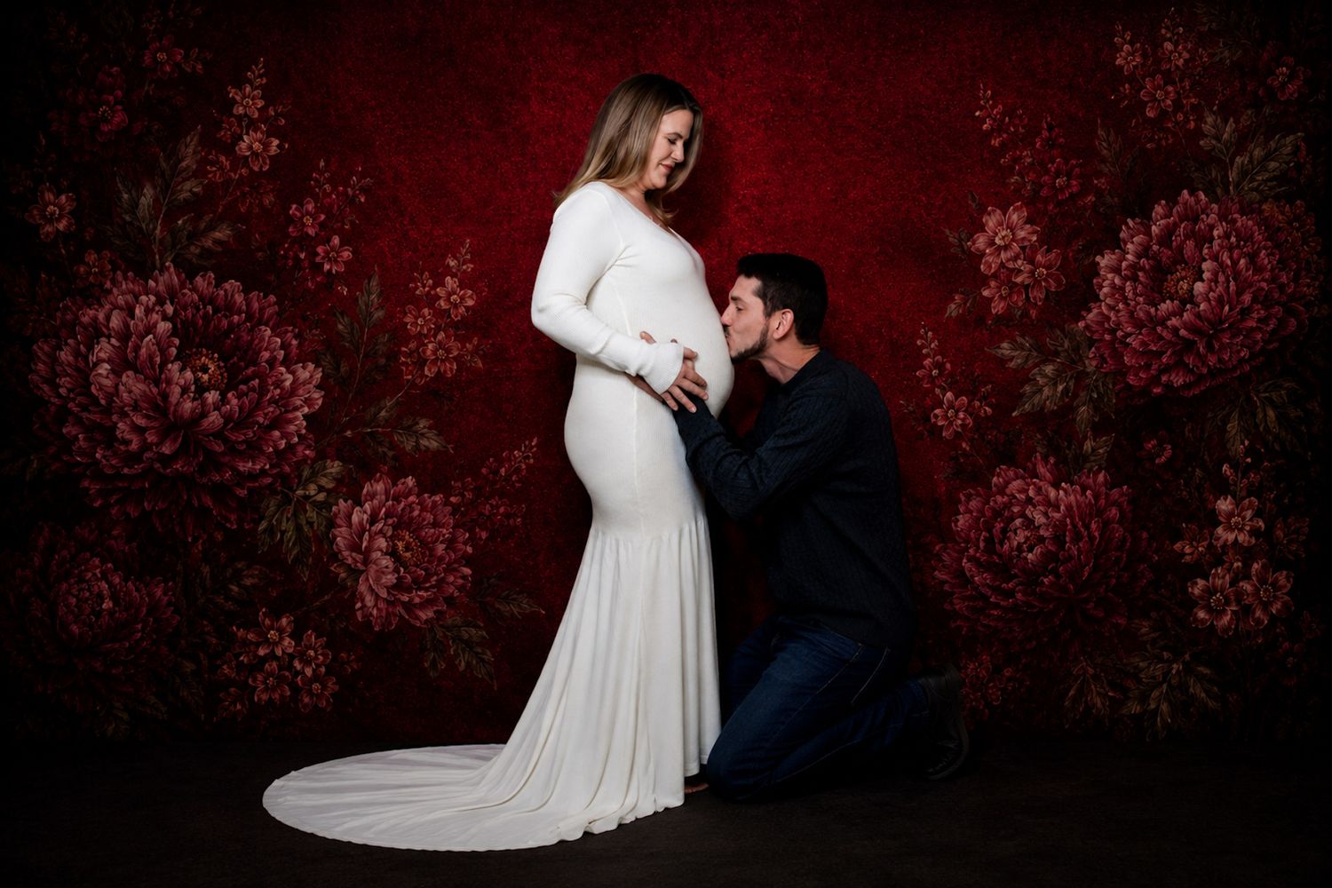 Halifax Maternity photographer Pregnant woman in white gown with partner kneeling beside her against a red floral backdrop