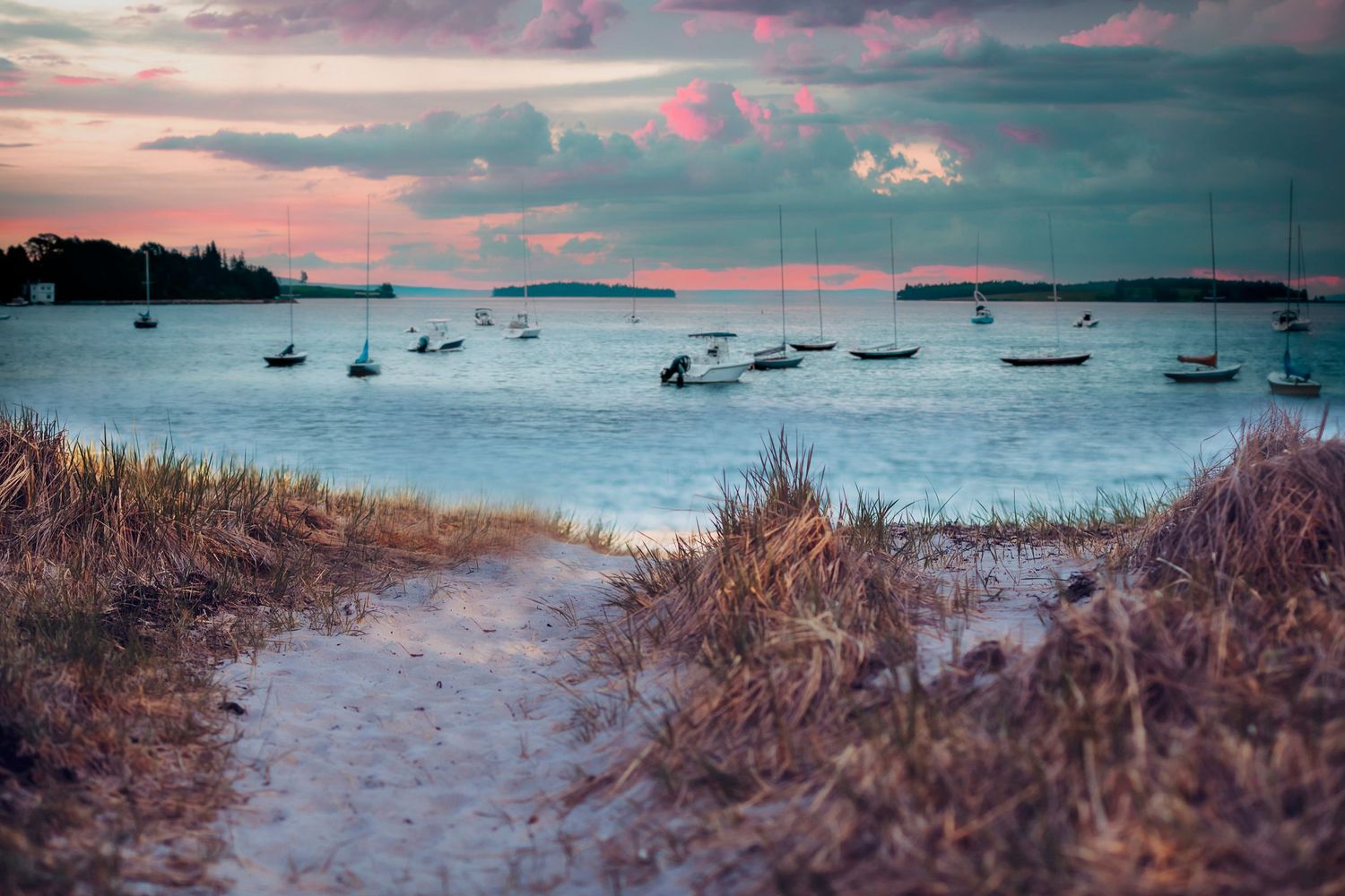in the Chester municipality Sandy path leading to a serene harbor at sunset with sailboats on calm water and dramatic pink clouds overhead.