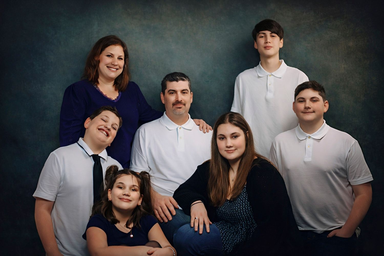 A family of seven poses for a professional portrait against a dark blue studio background.