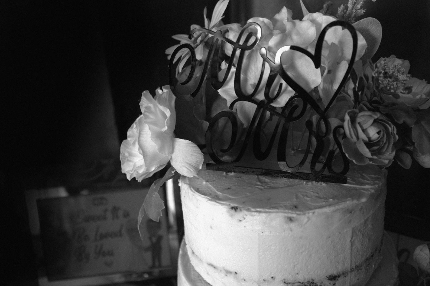 Black and white photo of a wedding cake with floral decorations and a decorative Mr & Mrs cake topper.