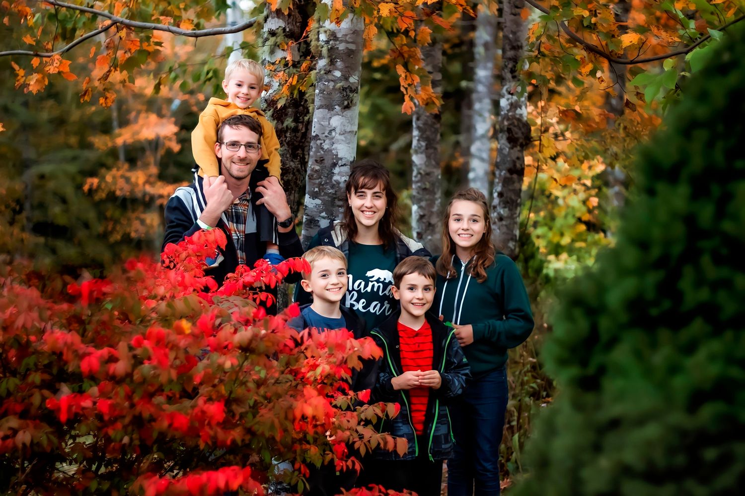 a Middleton Family of six posing outdoors among vibrant red and orange autumn foliage in a lush forest setting.