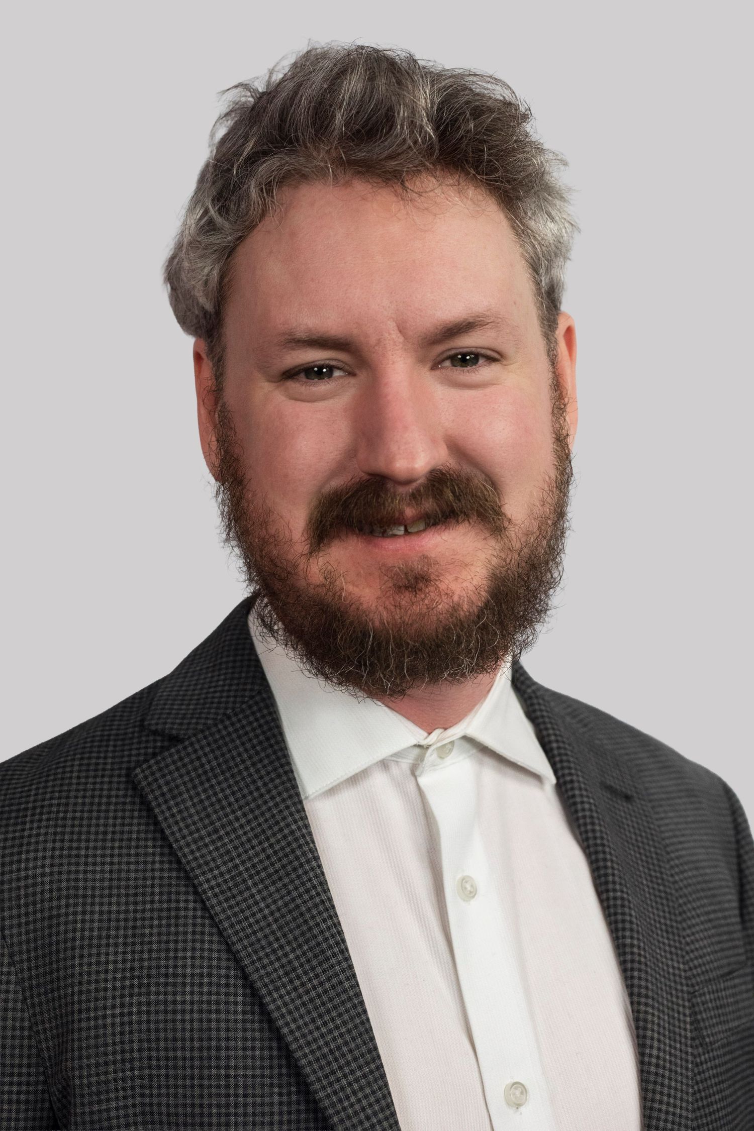 Professional headshot of a bearded man with gray-brown hair wearing a dark blazer and white shirt.
