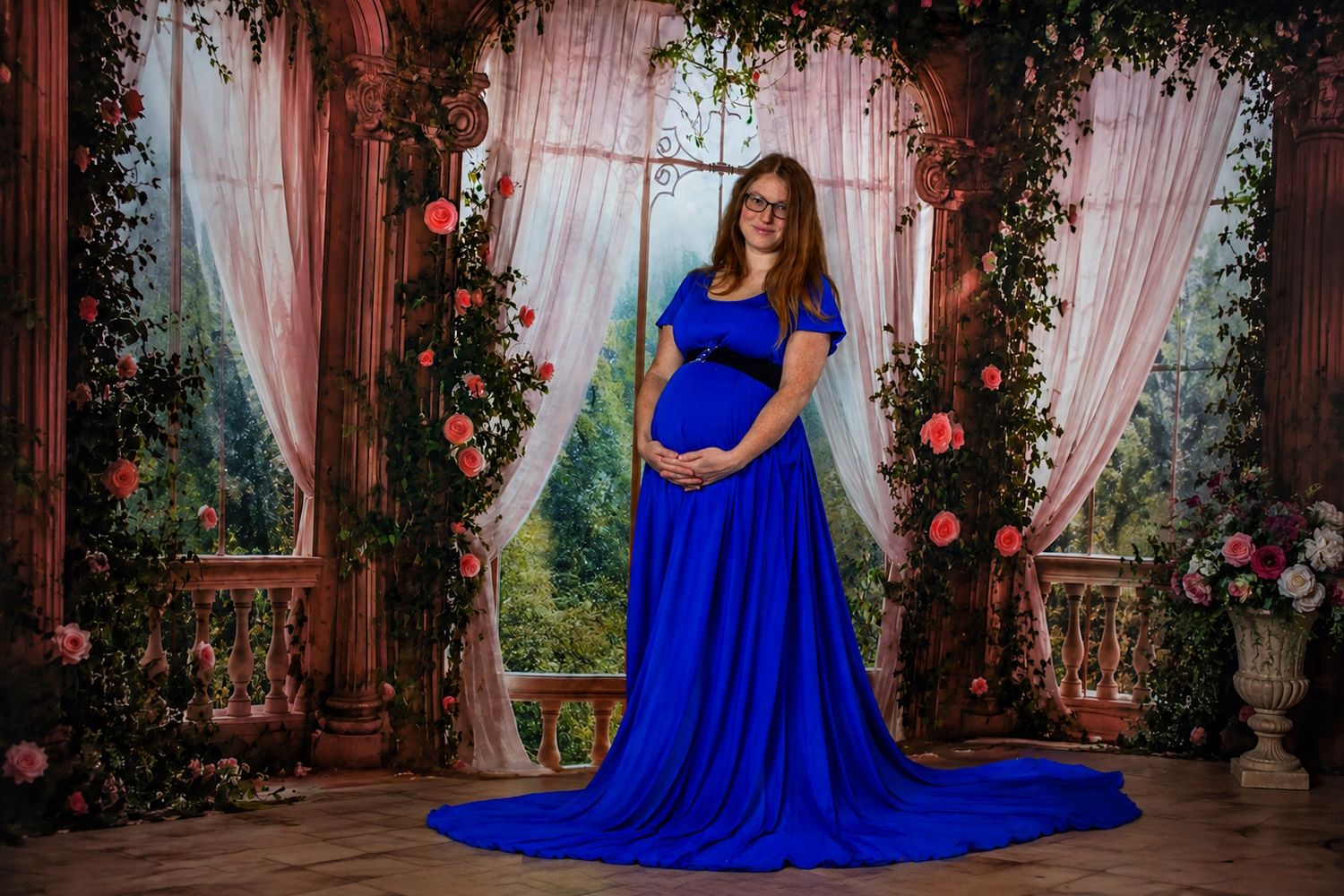 Halifax Nova Scotia Pregnant woman in royal blue maternity gown posing in floral studio setting with roses and curtains.