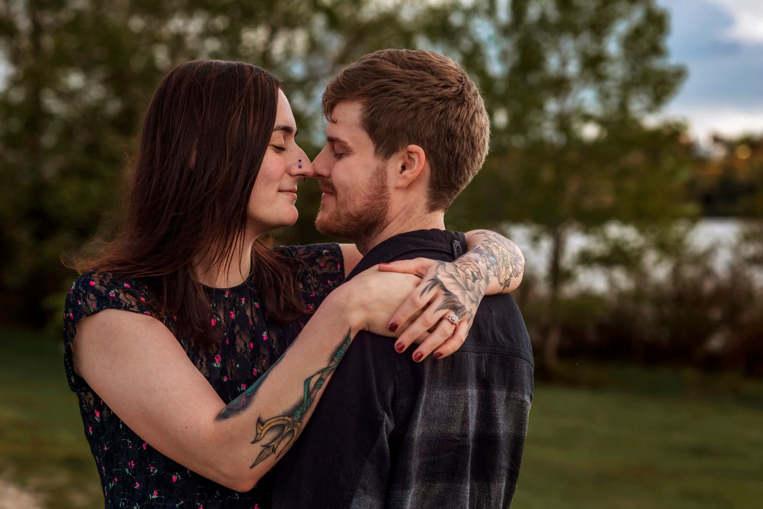 near Halifax A couple with tattoos shares a romantic moment outdoors, nearly kissing while embraced near a lake.