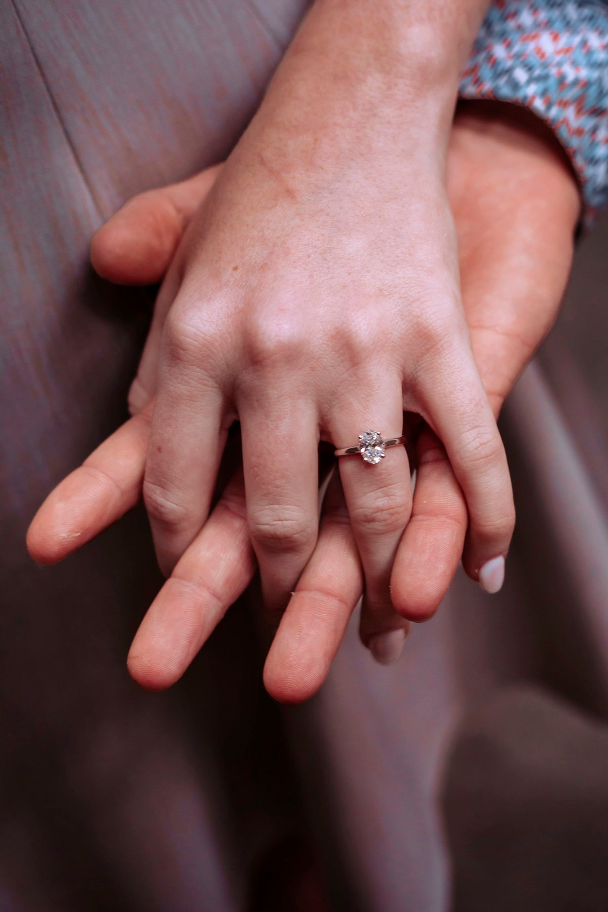 Two hands intertwined showing a sparkling diamond engagement ring on a woman's finger.