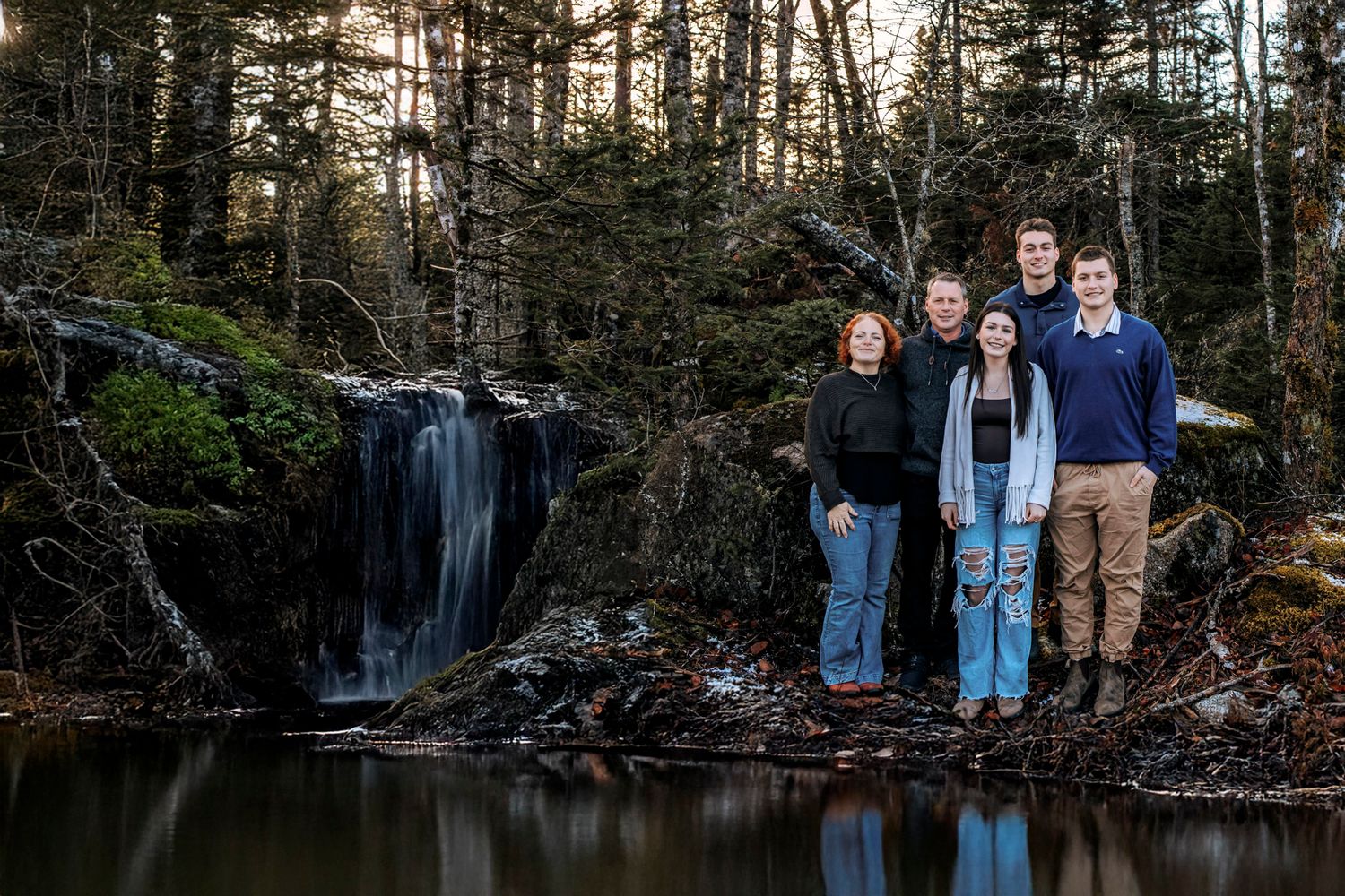 Middleton Family of five posing by a serene woodland waterfall and reflective pond surrounded by tall evergreen trees.