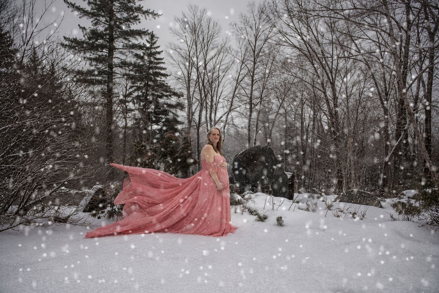 Woman in flowing pink gown twirling in snowy winter forest with snowflakes falling around her.