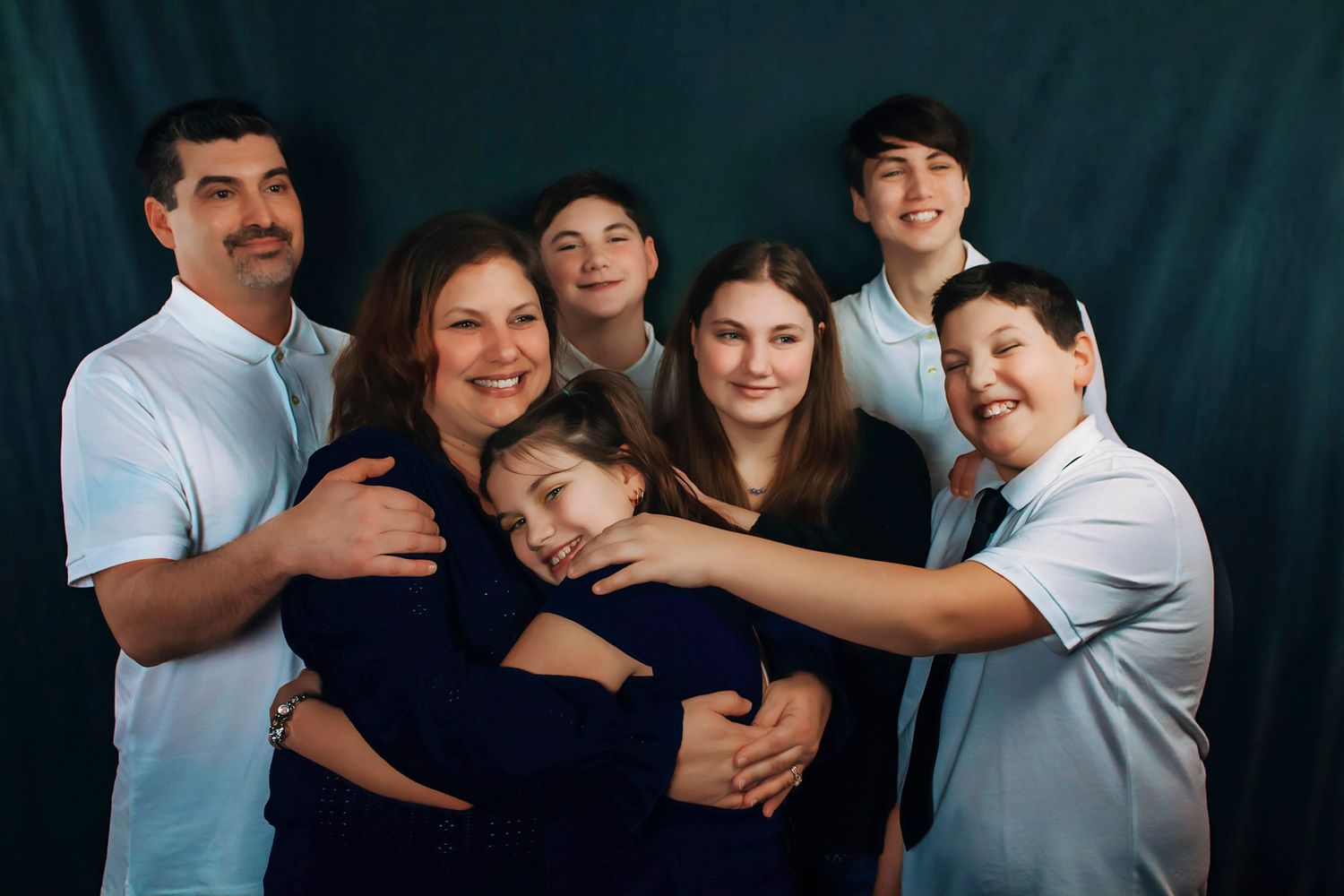 Nova Scotia Studio session, A joyful family of seven poses together, smiling and hugging against a dark teal studio backdrop in Nova Scotia