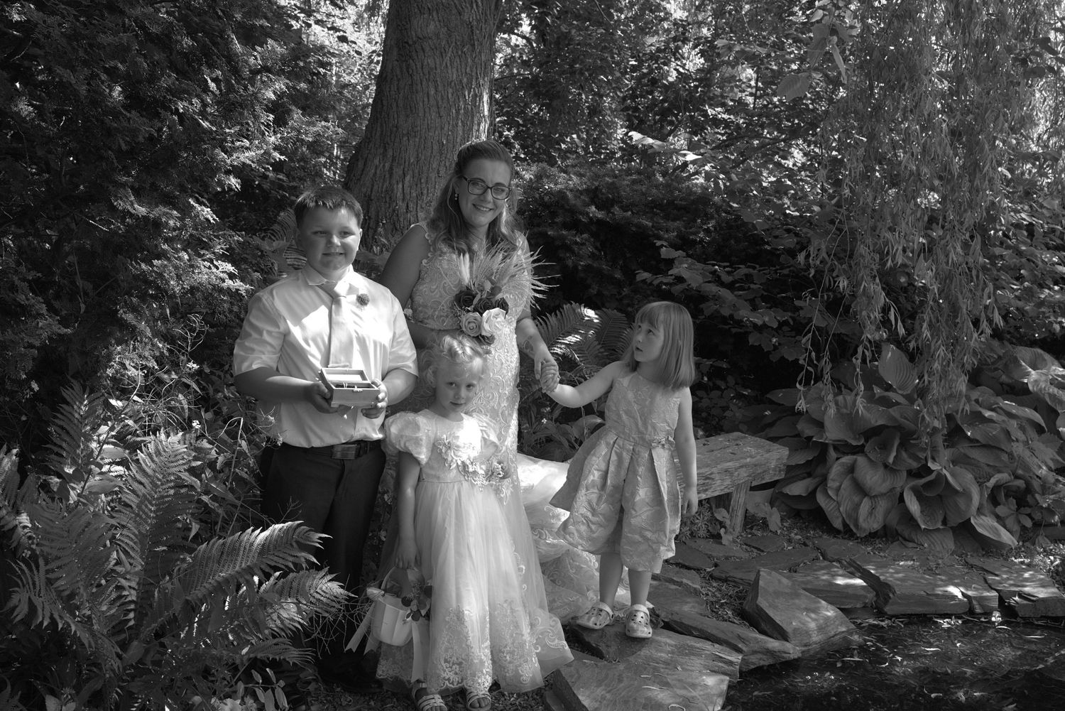 Black and white photo of a family with children posing outdoors in a lush garden near a small stream.