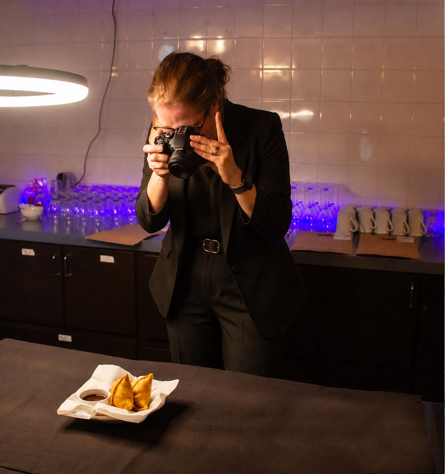 Photographer in black suit capturing food photography of fried appetizers on white plate in modern dark kitchen.
