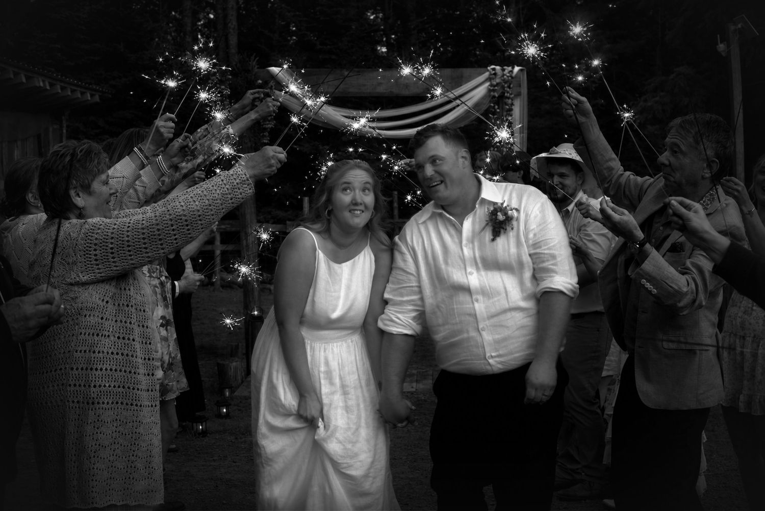 Black and white photo of a bride and groom walking through a sparkler exit at their wedding reception.