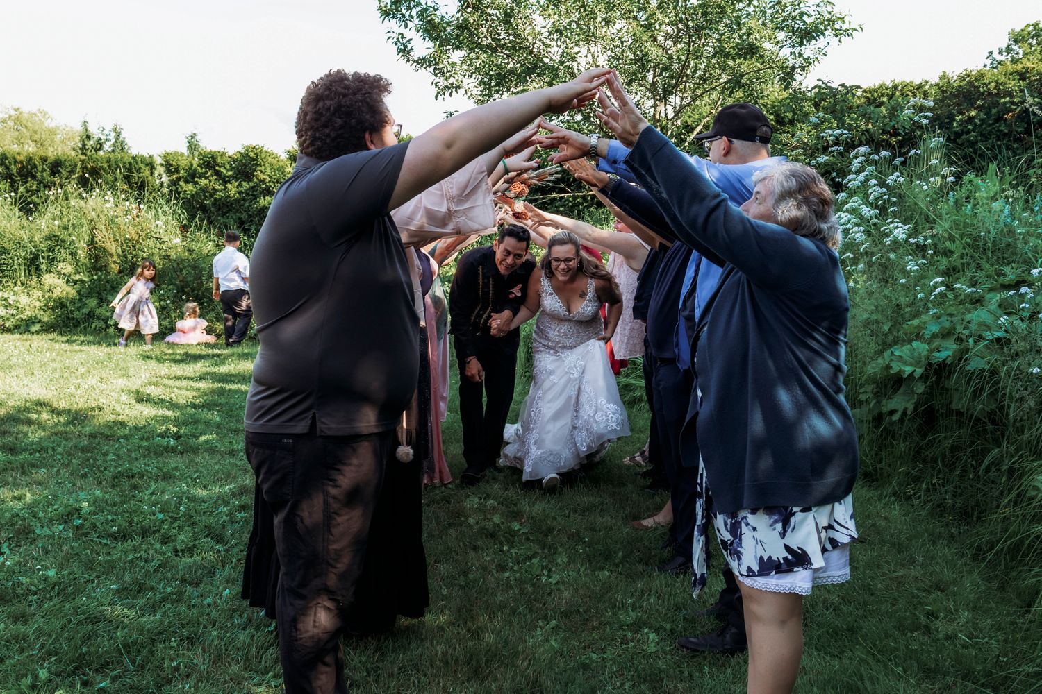 Wedding guests forming an arch with their arms as bride and groom walk through outdoor garden celebration.