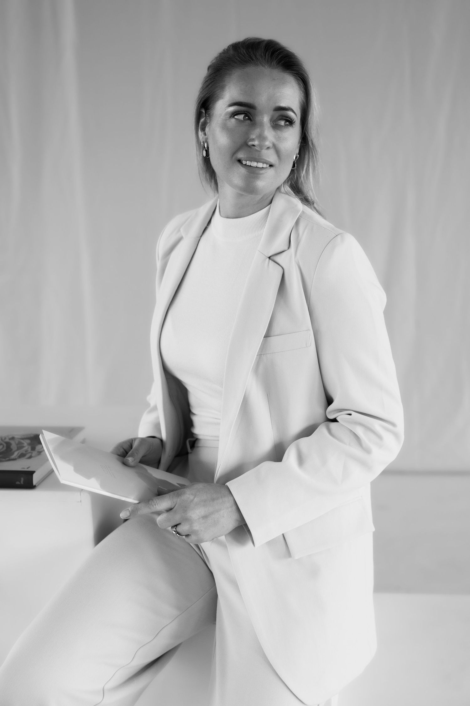 Black and white portrait of a smiling woman in a blazer holding a tablet, seated against a light background.