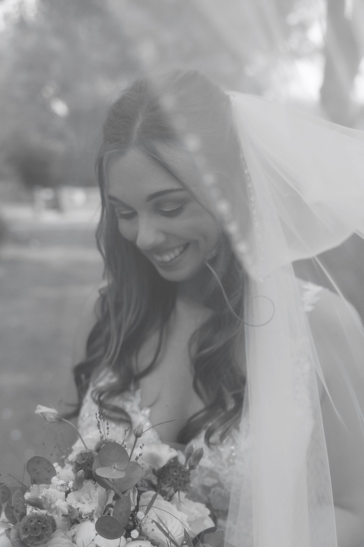 Smiling bride in veil holding bouquet, black and white wedding portrait photo.