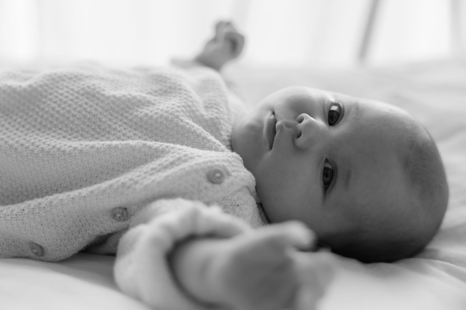 Black and white photo of a peaceful newborn baby lying on its back wearing a knit onesie.