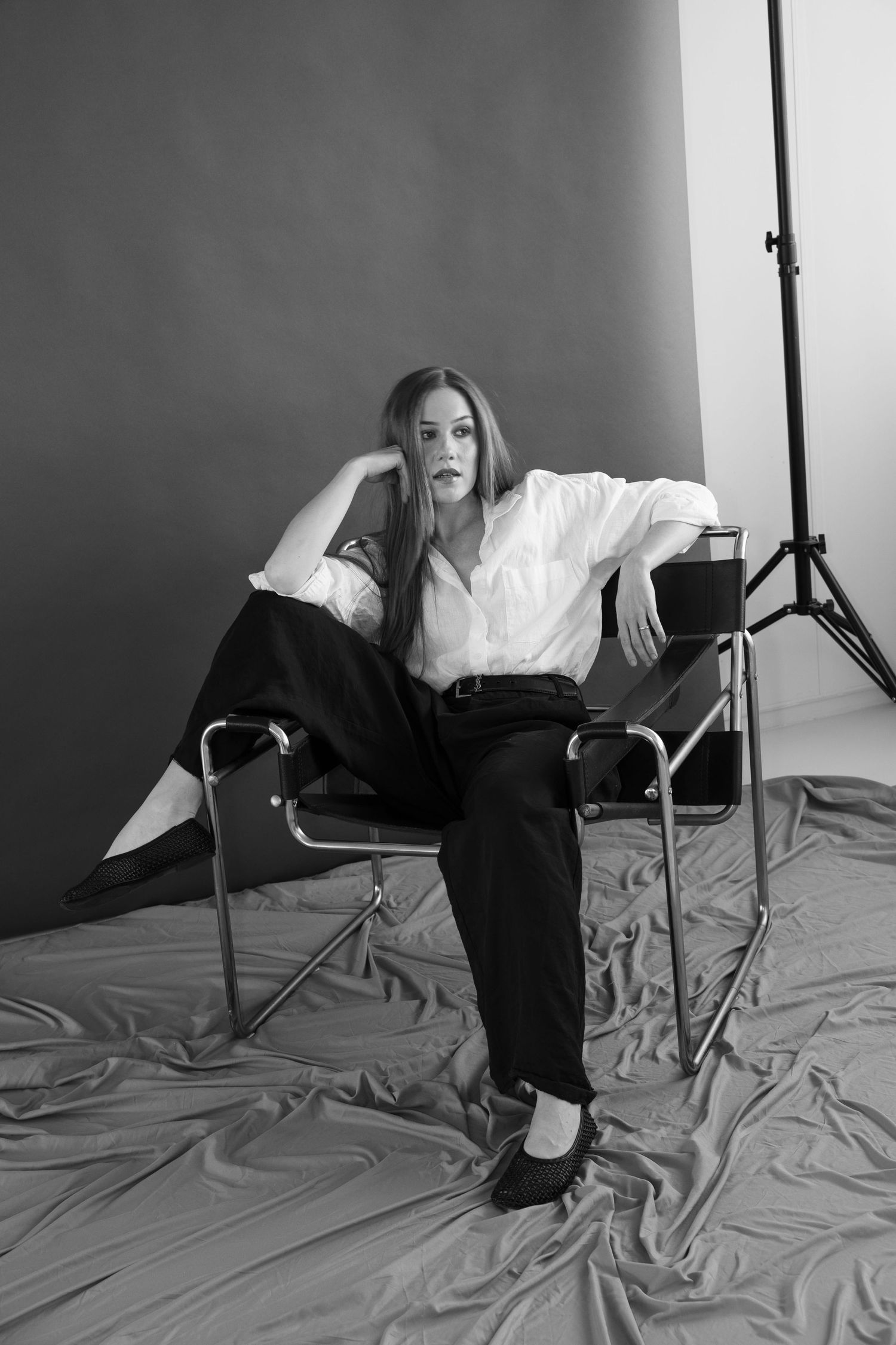 Black and white photo of a woman in white shirt and black pants sitting in a chair in a photography studio.