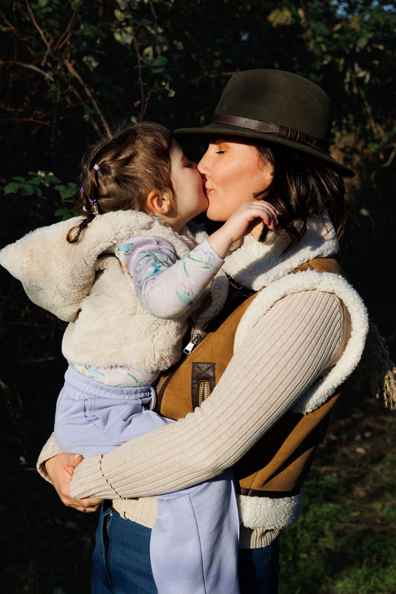 Sweet tender moment between parent and child wearing a warm brown hat and sweater vest on a sunny autumn day.