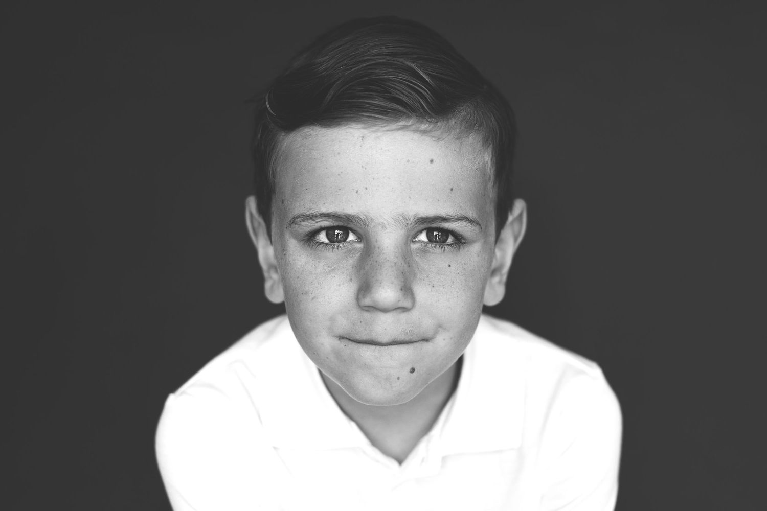 Black and white portrait of a young smiling boy with freckles wearing a white shirt.