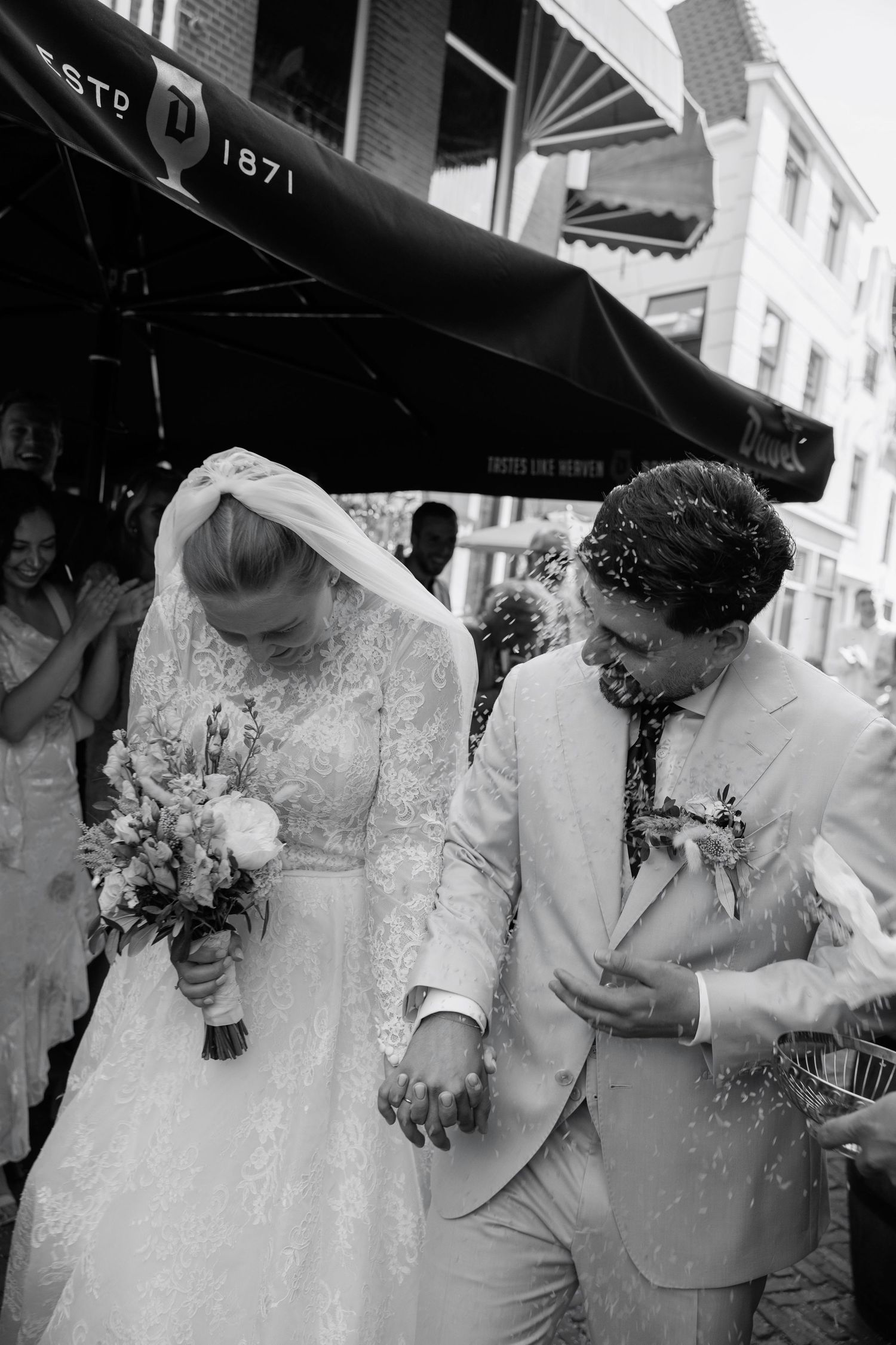 Black and white photo of a bride and groom exiting a venue as guests toss rice during their wedding celebration.