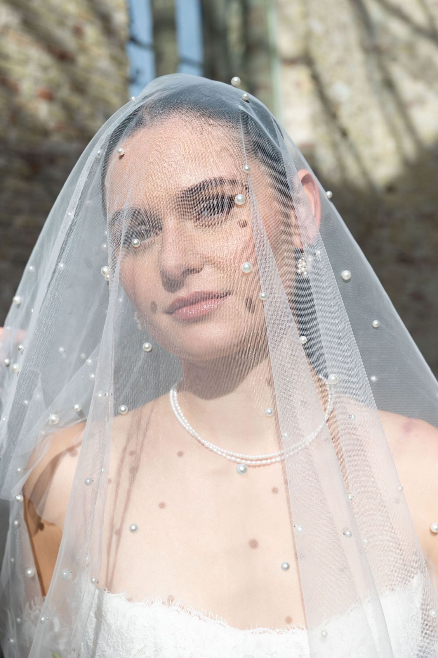 Bride wearing a pearl-embellished tulle veil with matching pearl necklace and earrings in a white strapless wedding gown.