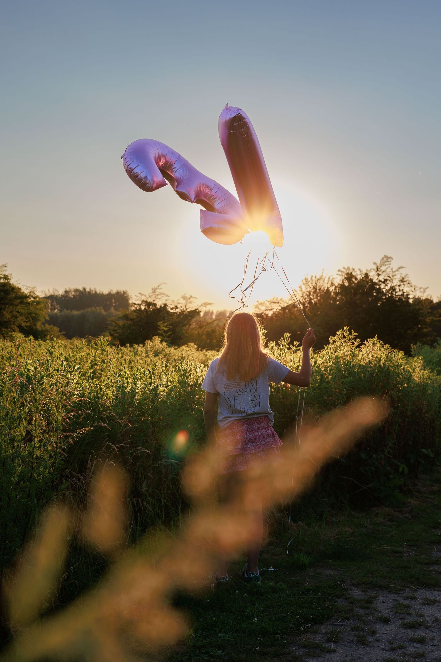 Silhouette holds heart-shaped balloons against golden sunset in wildflower field, creating dreamy summer atmosphere.